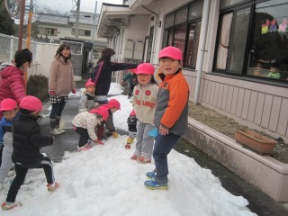 雪で出来た山の上に2人園児が昇っており、周りにも雪を触ったりして雪遊びをしている写真