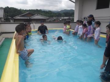 子どもたちがプール内でワニ歩きで泳ぐ練習をしている様子
