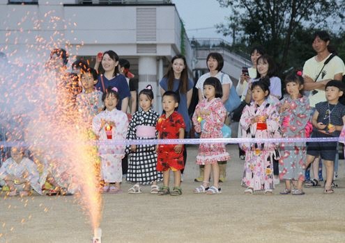 保護者と子どもたちが園庭で花火を見ている写真