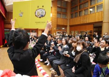 保育証書を受け取った園児が保育証書を参列者の保護者の方々に広げて見せている写真