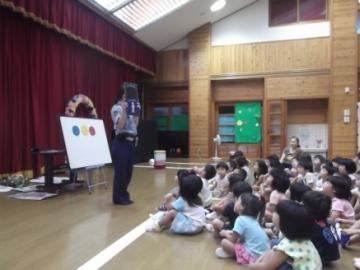 ホワイトボードの前に立って話をしている田辺警察署員と信号の話を聞いている子どもたちの写真