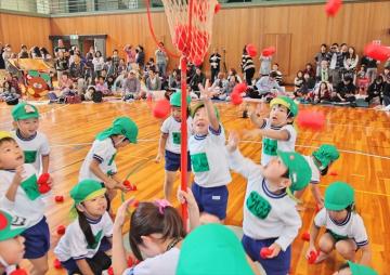 緑の帽子をかぶった園児が、赤いお手玉を投げて玉入れをしている写真