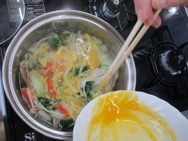 材料の煮立った鍋に溶き卵を加えている写真