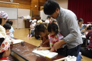 パパと一緒に麺棒で伸ばしたうどんを包丁で切っている子どもの写真