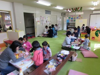 プレイルームで手作り体験などのワークショップに子供や大人が参加している写真