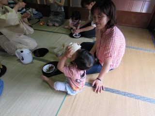 子どもが両手にお茶碗を持ちお茶を飲んでいる写真