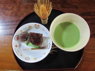 お盆にお抹茶とお菓子、茶せんがのっている写真