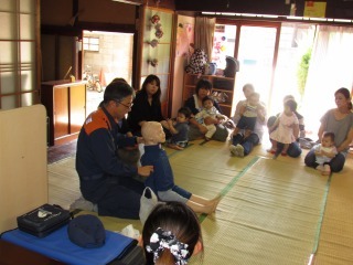 消防士が人形を使って説明をしていて、周りに座ったママ達が話しをきいている写真