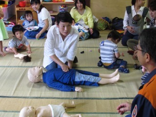一人のママが人形を使って消防士から心肺蘇生法を教えてもらっている写真