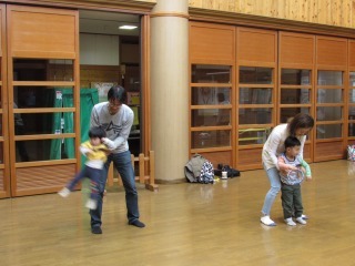 パパやママが子供を持ち上げて左右に揺らし、あそんでいる写真