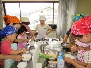 頭に三角巾を巻いて、エプロンをつけた親子がピザの生地を作っている写真