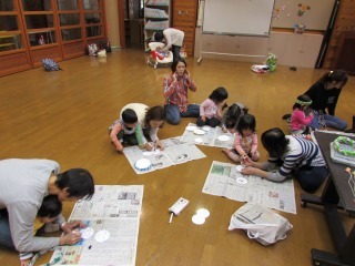 新聞紙の上ででんでん太鼓を作っている親子の写真