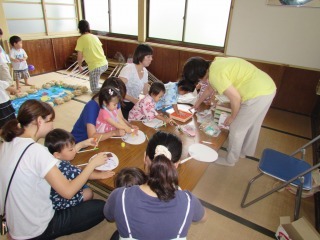 長机の周りに座った親子がうちわ作りをしている写真