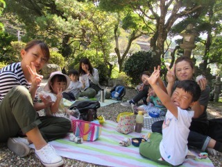 シートの上に座った親子がおにぎりを手に持ち、反対の手でピースサインをしている写真