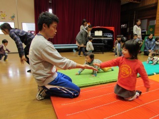 マットの上を歩いている子どもにお父さんが手を出している写真