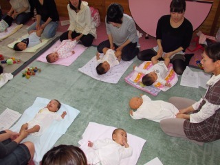 赤ちゃんを床に寝ころばせ、お母さんが赤ちゃんの手を持ちふれあいあそびをしている写真