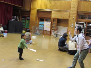 ママに羽を投げてもらって、小さい女の子が羽子板を持って、親子であそんでいる写真