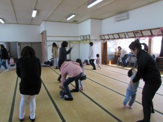 小さな子どもとママが手をつないで歩いたり、向い合ったりして、鬼ごっこをしている写真
