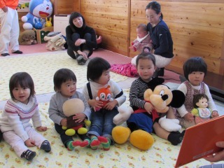 ぬいぐるみを抱っこした子どもたちが、絵本を観ている写真