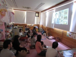 親子がスクリーンに映っている赤ちゃんの泣きについてのDVDを観ている写真