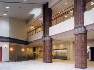 床から天井まで太く大きな柱が2本、二階から下のロビーが見下ろせるような造りになっている明るく開放的なロビーの写真