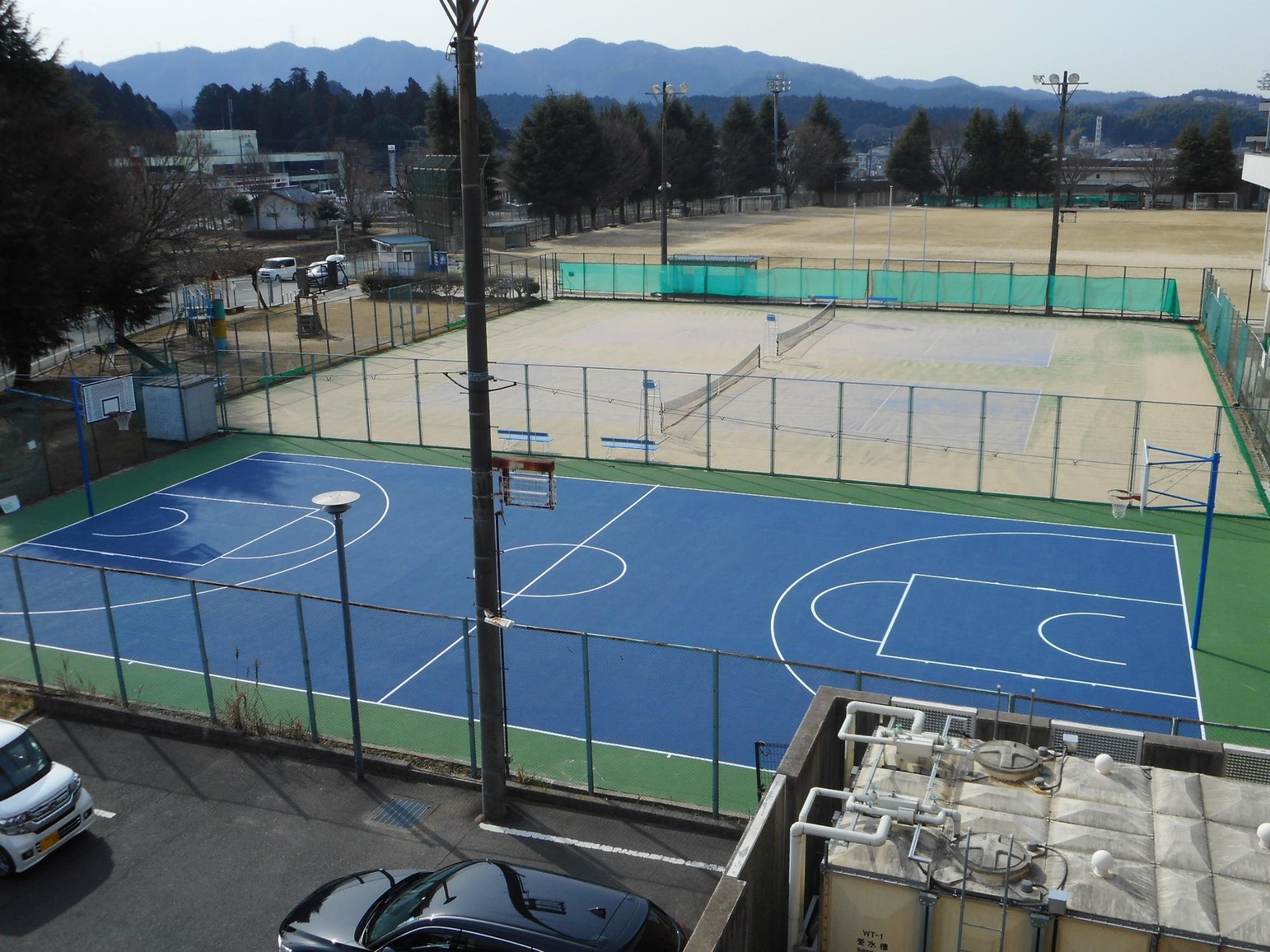 手前のバスケットコートのフェンスを挟んだ隣に設置されたテニスコートの写真