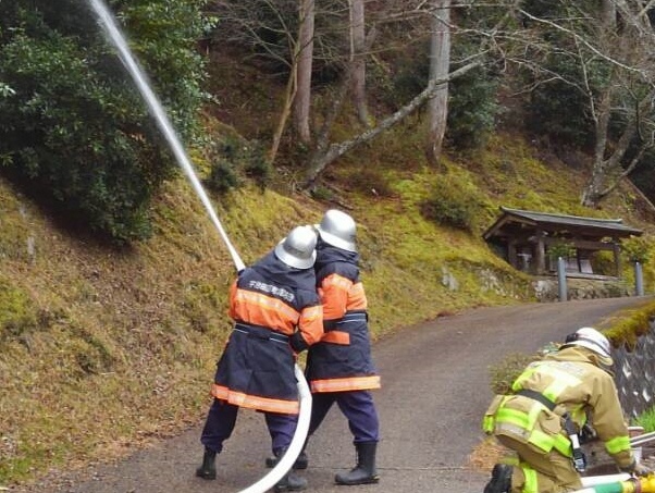 2名の消防団員が、木々が生えている方向に向かって放水をしている訓練の様子の写真