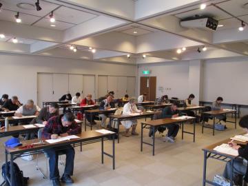 15個の長机に一人ずつ参加者が座って試験を受けている様子を斜め前から撮影した写真