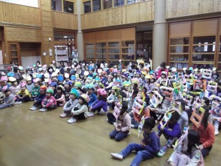 お面を被った子ども達がホールに集まって座っている節分集会のようすの写真