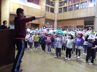 お面を被った子ども達が立ち上がって、両手を上に挙げて歌と踊りを楽しんでいる節分集会のようすの写真