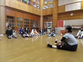 バレエ講師の高山さんと参加者の皆さんが向き合って、足を前に伸ばして座っており、子どもを膝の上に座らせている写真