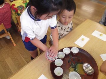 女の子がお盆にのっている茶碗にお茶を注いでいる写真