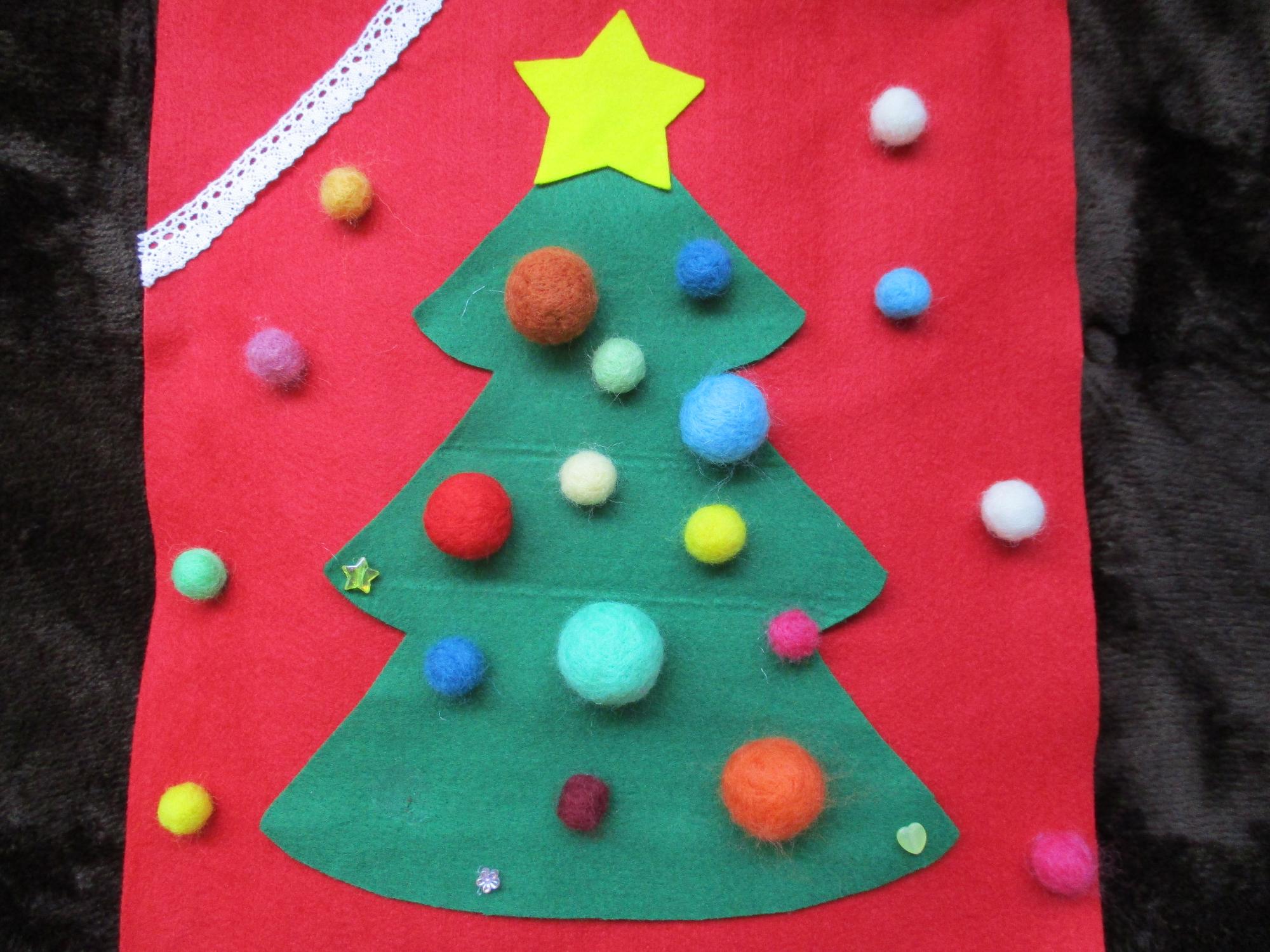 赤地に緑のクリスマスツリーと天辺の星がかわいい壁に飾られたクリスマスのタペストリーの写真