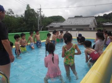 子どもたちがプール手で水をすくって、息を吹きかける練習をしている様子の写真