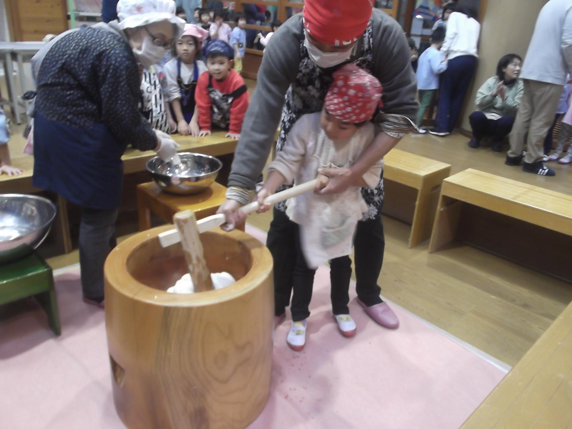 おじいちゃんおばあちゃんと子どもが一緒にもちつきをしている様子の写真