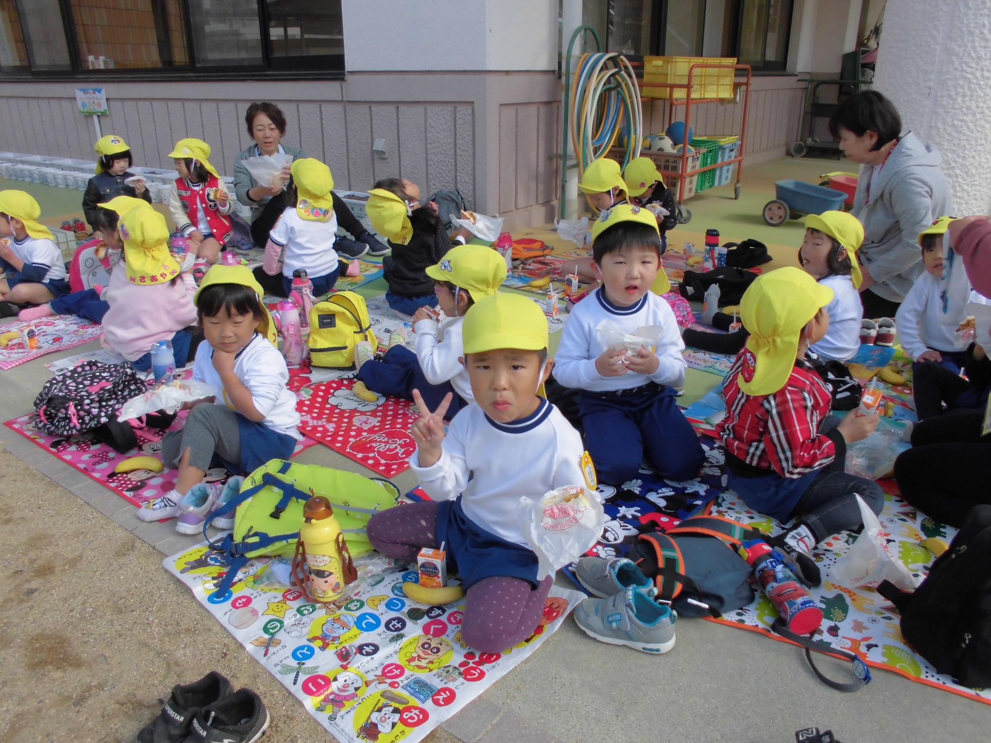 園庭でコロッケバーガーを食べている子ども達の写真