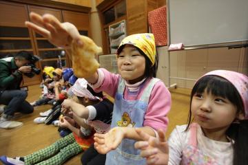 エプロンをつけた子どもが手に持ったおもちを見せている写真