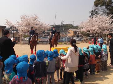 馬に乗った2人の女性警察官の前に、横一列に並んで立っている子どもたちの写真