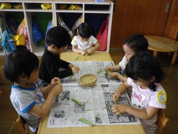 新聞紙を広げた机の上で、子ども達がえんどう豆のさやをむいている写真