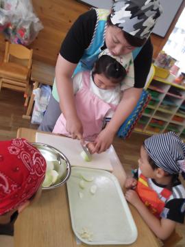 子どもが食育指導協力者の女性と一緒に玉ねぎを切っている写真