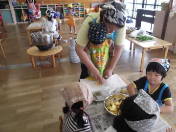 大人に手伝ってもらいながら子どもが野菜を切っている写真