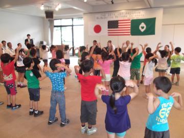 壁に日本やアメリカの国旗が掲げられた室内で子供たちがダンスを踊っている写真