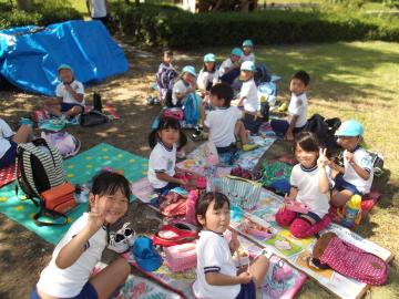 子ども達が敷物の上でお弁当を食べている写真