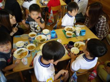 給食を食べている子どもたちとその様子を傍で見ている保護者の写真