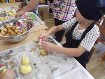 三角巾とエプロンを身につけた子どもが野菜の皮むきをしている写真