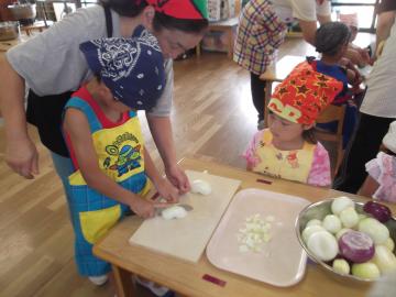 包丁を使って野菜を切っている子供と後ろから補助している先生の写真