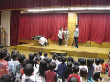舞台上で劇を演じる先生と劇を見ている子どもたちの写真