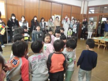 保護者や家族の前で、子どもたちが集まり、わらべうたを歌っている写真