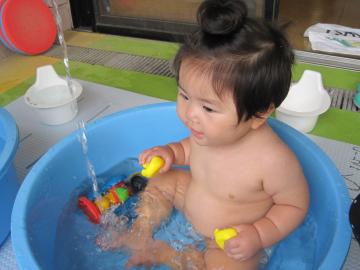 0歳児の子どもがタライの中で水遊びをしている写真