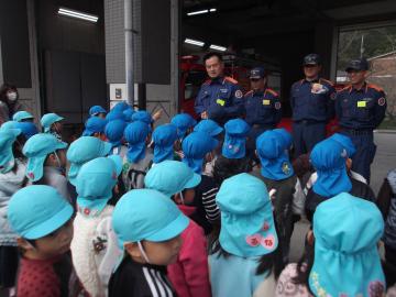 青と水色の帽子をかぶった園児が、前方に立つ消防団の男性4名の前に並んでいる写真